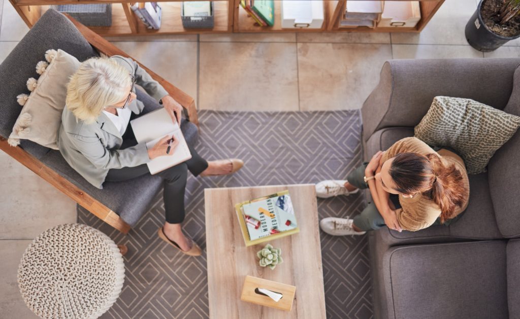 Top view, psychologist and patient woman in consultation office, lounge sofa or talking for anxiety