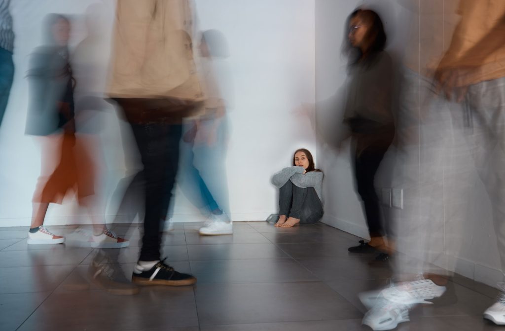 A woman with schizophrenia sitting in the corner of a crowded room.